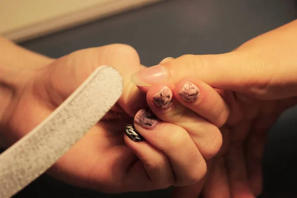 A student at the training courses of a manicure prepares the hand of a lady client with a file before applying shellac.