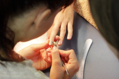 Manikür kursunda okuyan bir öğrenci, Shellac uygulamadan önce kazıyıcı aletle bir bayan müşterinin elini hazırlar.