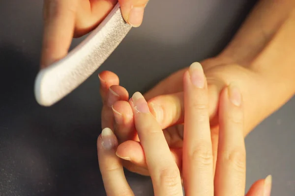 A student at the training courses of a manicure prepares the hand of a lady client with a file before applying shellac