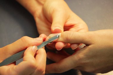 Manikür kursunda okuyan bir öğrenci, Shellac uygulamadan önce kazıyıcı aletle bir bayan müşterinin elini hazırlar.