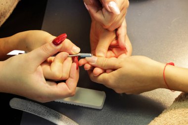 Manikür kursunda okuyan bir öğrenci, Shellac uygulamadan önce kazıyıcı aletle bir bayan müşterinin elini hazırlar.