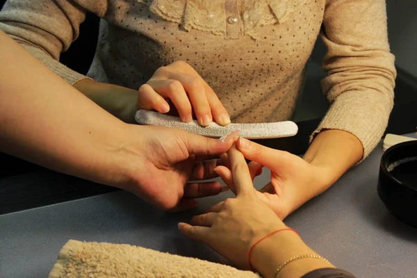 A student at the training courses of a manicure prepares the hand of a lady client with a file before applying shellac