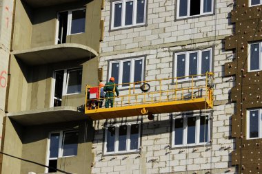 Sarı ön taraftaki iki askıya alınmış beşikte yeni inşa edilmiş bir binanın işçileriyle çalışmak..