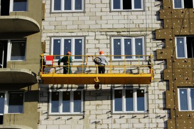 Sarı ön taraftaki iki askıya alınmış beşikte yeni inşa edilmiş bir binanın işçileriyle çalışmak..