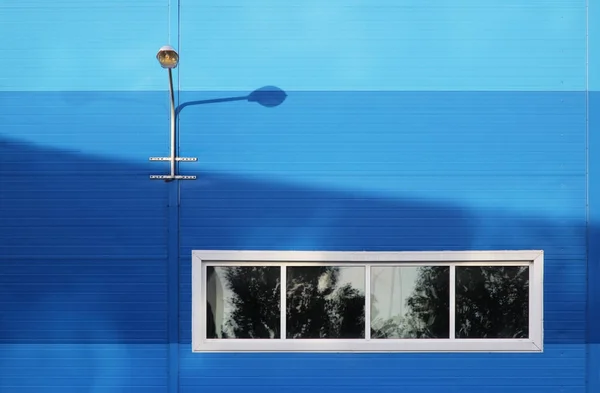 The surface of the blue wall of a large office building. There are four windows. wall lamp for street lighting.