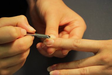 Manikür kursunda okuyan bir öğrenci, Shellac uygulamadan önce kazıyıcı aletle bir bayan müşterinin elini hazırlar.