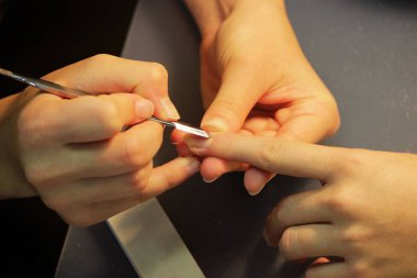 Manikür kursunda okuyan bir öğrenci, Shellac uygulamadan önce kazıyıcı aletle bir bayan müşterinin elini hazırlar.