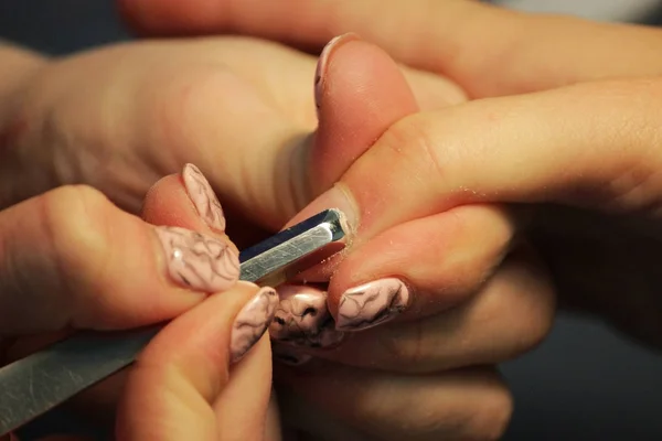 A student at the training courses of a manicure prepares the hand of a lady client with tool for scraping scraper before applying shellac