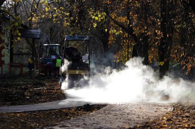 yol mini bina silindiri onarım sitenin yanındaki kaldırımda bisiklet yolunun üzerinde çalışıyor. Beyaz buharı yanıyor güneşte.