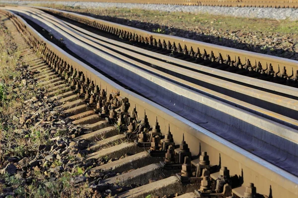 Kilka szyny leżą na podkładach między przekrojami na kolei. śruby mocujące szyn do podkładów na kierunek kolejowe — Zdjęcie stockowe