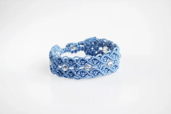 Bracelet bleu pour la main à partir de fil ciré, et perles en plastique transparent dans la technique du macramé sur un fond blanc. Fait à la main . — Photo