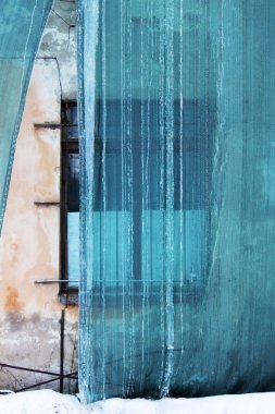 Bina ve koruyucu bir yeşil mesh çatıdan süzülmüş donmuş su ile bina restorasyonu. Eski pencere