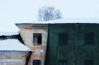 Bina ve koruyucu bir yeşil mesh çatıdan süzülmüş donmuş su ile bina restorasyonu. Eski pencere