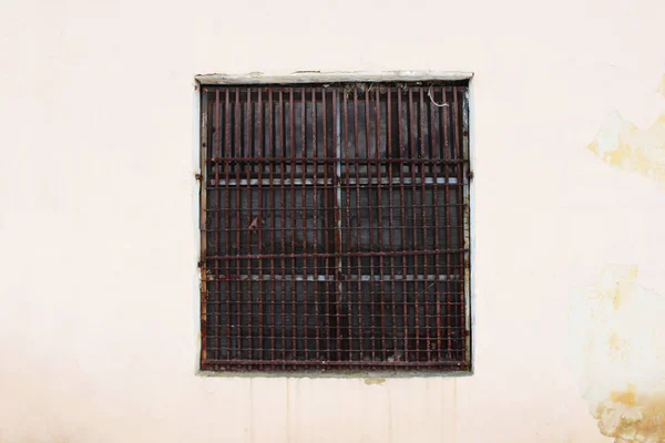 beige wall with a square window behind a thick rusty old grate for background.