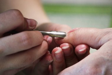 Manikür kursunda okuyan bir öğrenci, Shellac uygulamadan önce kazıyıcı aletle bir bayan müşterinin elini hazırlar.