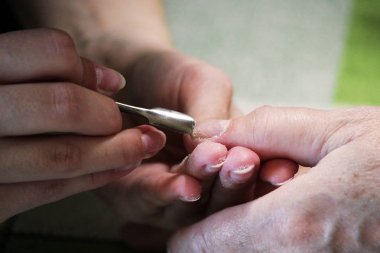 Manikür kursunda okuyan bir öğrenci, Shellac uygulamadan önce kazıyıcı aletle bir bayan müşterinin elini hazırlar.