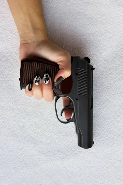 Mão de uma jovem mulher com uma arma em um fundo cinza. vertical . — Fotografia de Stock