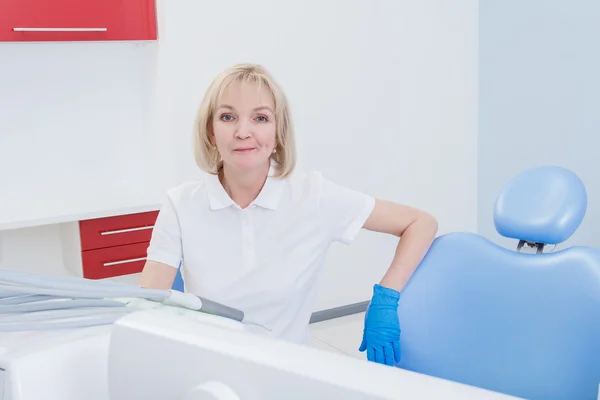 Dentista mulher com cabelo loiro sentado em uma cadeira no consultório odontológico — Fotografia de Stock