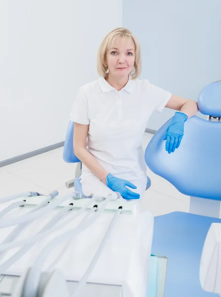 Стоматолог-жінка зі світлим волоссям сидить на стільці в стоматологічному кабінеті — стокове фото