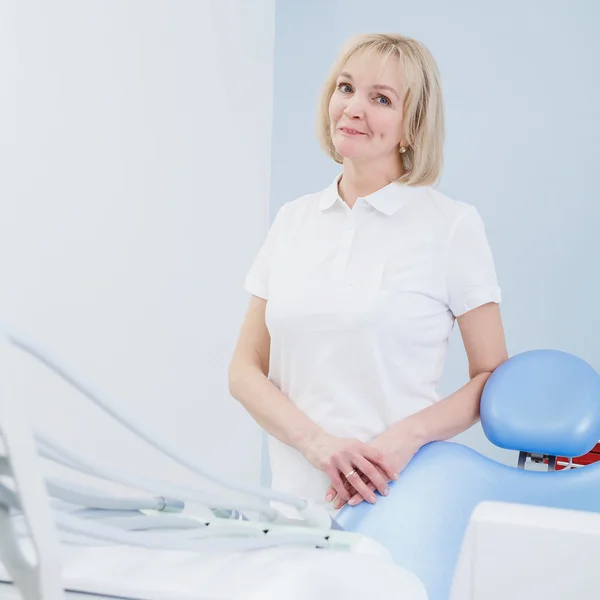 Стоматолог-жінка зі світлим волоссям стоїть біля стільця в стоматологічному кабінеті — стокове фото