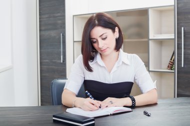 ofiste masada oturan bir siyah ve beyaz bluz giyen çekici esmer kadın.
