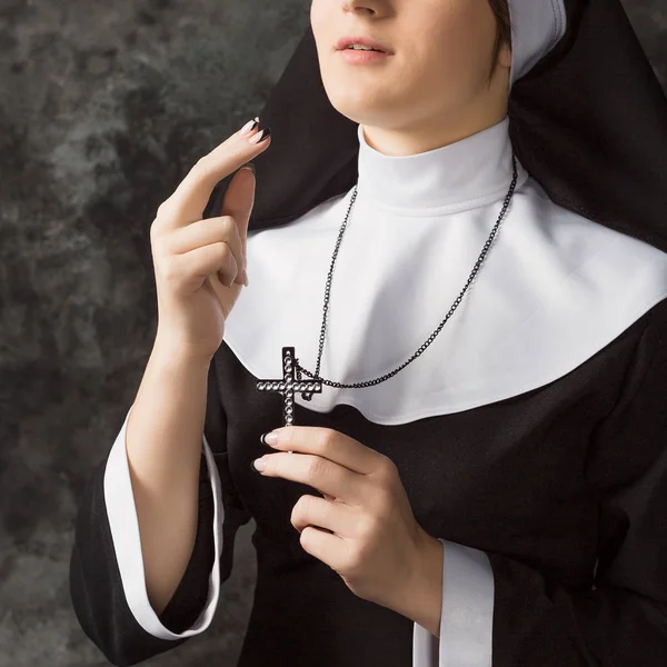 Monja joven con túnicas sosteniendo una cruz y el signo de la contra la pared oscura. Primer plano — Foto de Stock