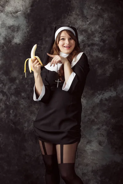 性感的修女，拿着一根香蕉和黑底色上显出他的手指的特写镜头。女人吃一根香蕉 — 图库照片