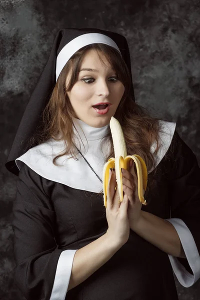 Κοντινό πλάνο της σέξι καλόγρια κρατώντας τα χέρια Eyad μπανάνα και θαύματα της ντροπής σε σκούρο φόντο. Γυναίκα τρώει μια μπανάνα — Φωτογραφία Αρχείου