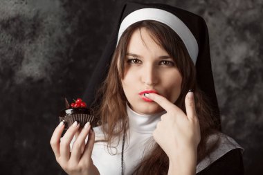 attractive nun holding a chocolate cake with berries on a dark background.woman licks her finger clipart