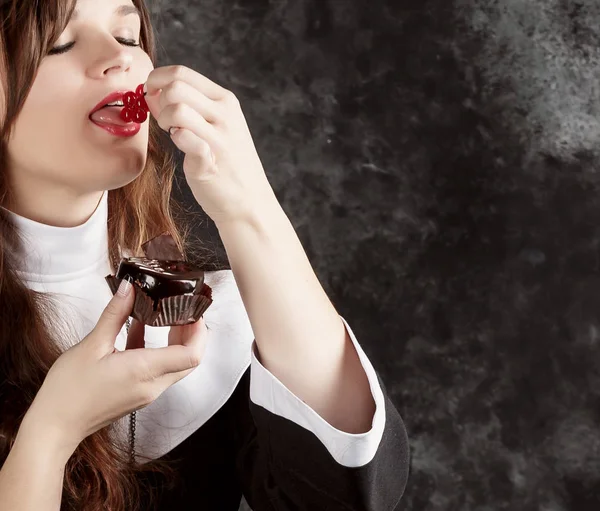 Jolie religieuse tenant un gâteau au chocolat avec des baies sur un fond foncé.femme manger des groseilles — Photo