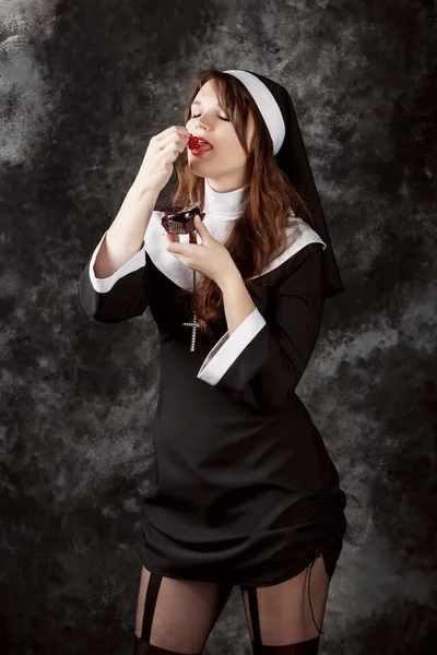 Freira atraente segurando um bolo de chocolate com bagas em um fundo escuro. — Fotografia de Stock