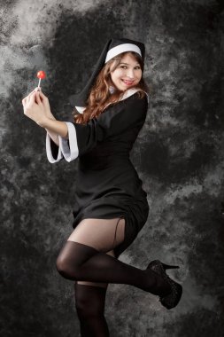 young sexy stockings nun holding a red candy on a dark background.attractive brunette girl with bonbon lifted one leg clipart