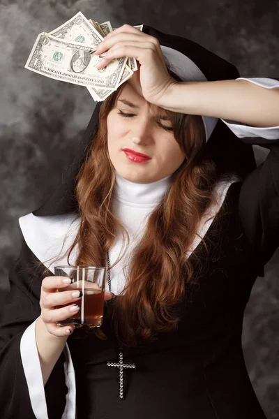 Porträt einer Nonne mit Dollarscheinen und einem Glas Alkohol auf dunklem Hintergrund — Stockfoto