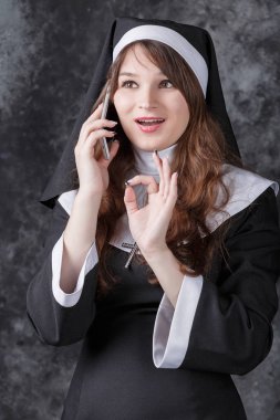 Karanlık bir arka plan üzerinde bir cep telefonuyla konuşurken Rahibe