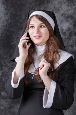 Karanlık bir arka plan üzerinde bir cep telefonuyla konuşurken Rahibe