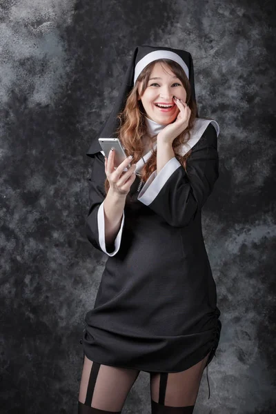 Freira uso retornar telefone celular e sorrindo em um fundo escuro . — Fotografia de Stock