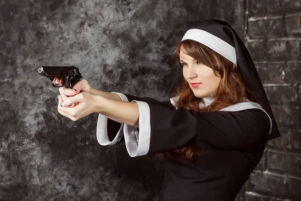 Monja sosteniendo una pistola sobre un fondo oscuro . — Foto de Stock