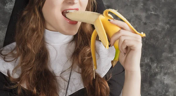Freira segurando uma banana e morde-o em um fundo sombrio.close-up . — Fotografia de Stock