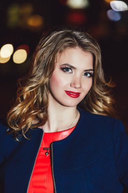 Güzel sarışın mavi ceket ve gece şehir ışıkları bir arka plan üzerinde kırmızı bir elbise içinde