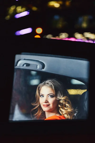 Потрясающая блондинка в машине ночью. Женщина на заднем сиденье машины на фоне ночного пожара. — стоковое фото