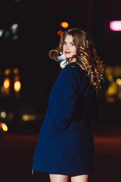 Красива блондинка в синьому пальто і червона сукня на фоні нічних міських вогнів — стокове фото