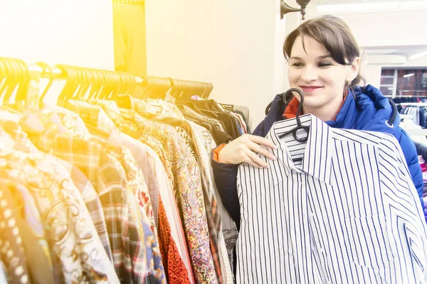 Młoda brunetka Kobieta w Błękitnej Kurtki wybiera ubrania w sklepie. Kobieta kupuje ubrania — Zdjęcie stockowe