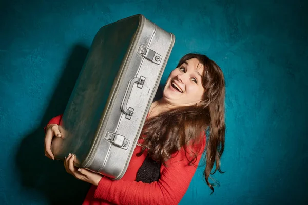 Mladá bruneta žena držící velký starý kufr na pozadí modré zdi — Stock fotografie