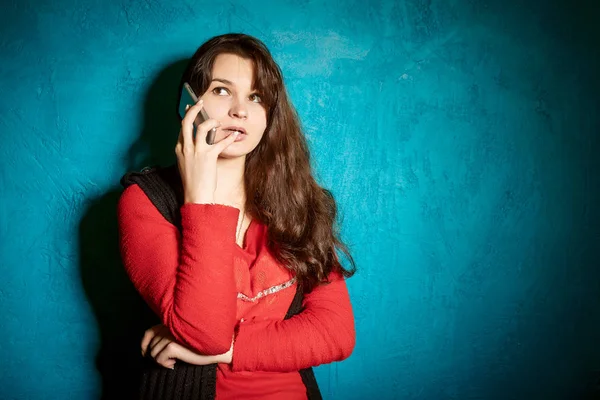Emotional young brunette woman talking on the phone on the background of blue wall — Stock Photo, Image