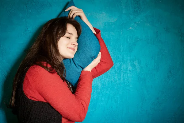 brunette woman in a red blouse leaning against a pillow in the blue wall and sleeps. Young woman sleeping on a pillow