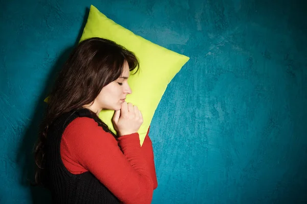 Брюнетка в красной блузке прислонилась к подушке в синей стене и спит. Молодая женщина спит на подушке — стоковое фото