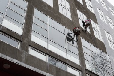 Üst pencere contalar. İki işçi ipleri yıkama windows yüksek katlı üzerinde asılı