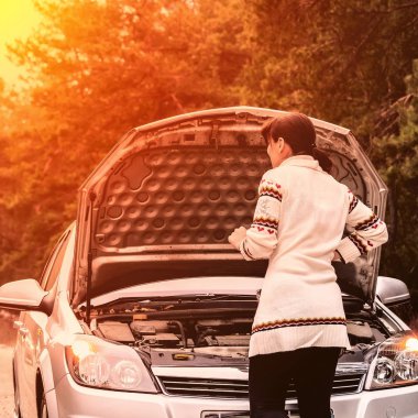 kırık arabanın yakınında duran genç kadın. Kız başlık açılmış ve motora bakmak. Kadın araba tamir