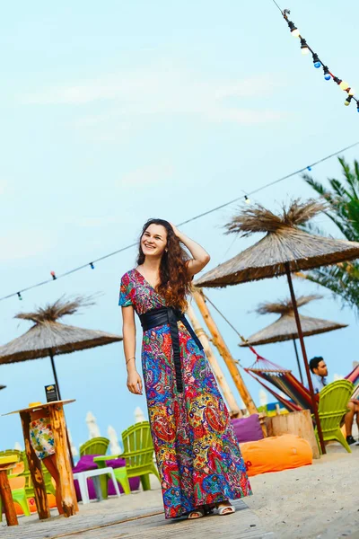 Bela morena em um vestido longo na praia perto do bar ou ir dançar. Conceito de entretenimento e recreação — Fotografia de Stock