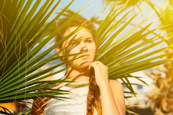 Atraktivní brunetka žena v bílých šatech stojící na pozadí Palmový list — Stock fotografie